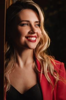 a beautiful girl dressed in a red formal suit posing in a modern interior.