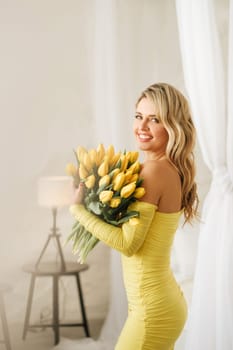 a happy woman in a yellow dress embraces a bouquet of yellow spring tulips in the interior.