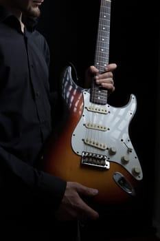Electric guitar in the hands of a man on black background.