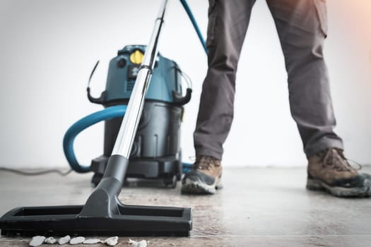 Close-up on the legs of a worker and the brush of a construction vacuum cleaner at a construction site.