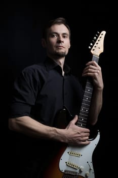 Studio low key portrait of guitarist with electric guitar with classic dark lighting.