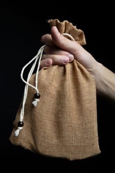 Human holding linen bag with laces in hands on black background.