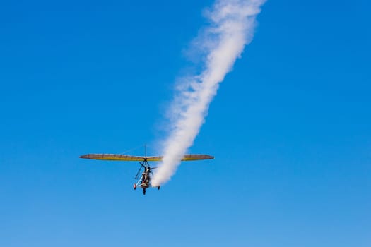 A paraglider with a cradle on wheels leaves a white trail in the blue sky.