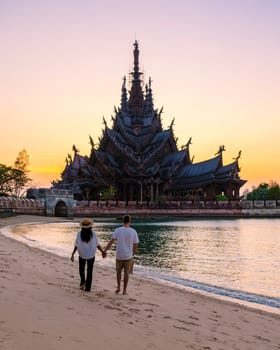 A couple of men and women visiting the Sanctuary of Truth, Pattaya, Thailand, wooden temple by the ocean during sunset on the beach of Pattaya. Temple of Truth in Thailand