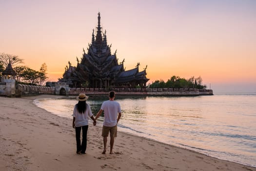 A couple of men and women visiting the Sanctuary of Truth, Pattaya, Thailand, wooden temple by the ocean during sunset on the beach of Pattaya. Temple of Truth in Thailand