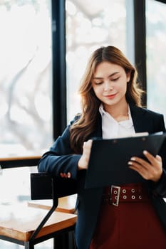 portrait of Beautiful young asian businesswoman presents business profits to colleagues at meeting, explaining business turn over on flipchart to coworkers in office with using tablet.