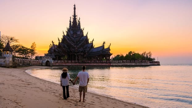 A couple of men and women visit the Sanctuary of Truth, Pattaya, Thailand, wooden temple by the ocean during sunset on the beach of Pattaya.