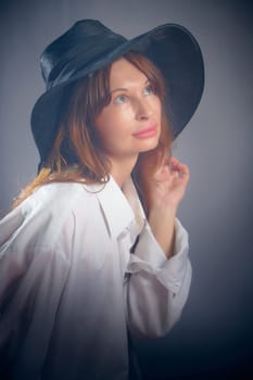 Portrait of a young sexy girl in white shirt and hat on a grey background. Classic style. dramatic portrait