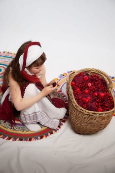 Portrait of Little girl in a stylized Tatar national costume with a large basket of red berries on a white background in the studio. Photo shoot of funny young teenager who is not a professional model