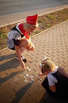 Young and adult schoolgirl on September 1 drawing by chalk on asphalt. Generation of schoolchildren of USSR and Russia. Female pioneer in red tie and October girl in modern uniform. Daughter and mom