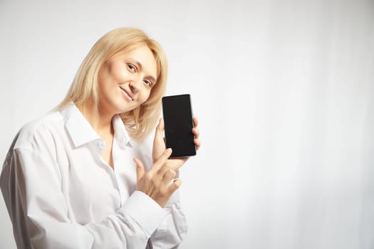 Portrait of a smiling casual woman holding smartphone over white background. The girl is chatting and taking selfies. Business lady with cell phone. Copy space