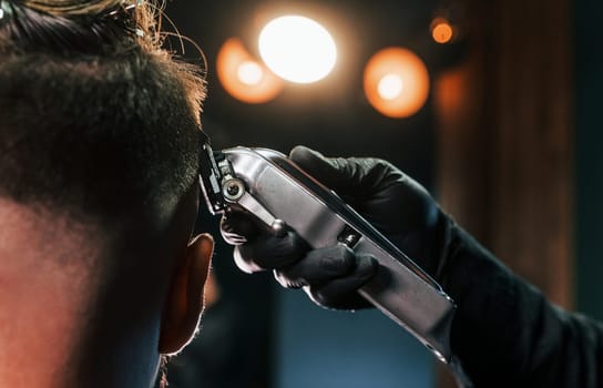 Close up view of young bearded man that sitting and getting haircut in barber shop.