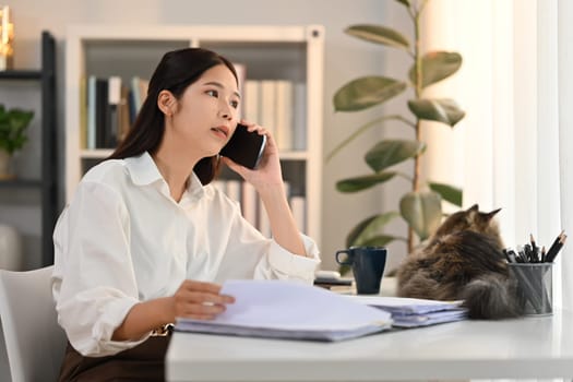 Confident adult female financial advisor consulting client distantly by mobile phone call, sitting at her workplace.