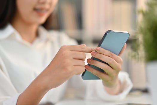 Selective focus on hands. Smiling young woman typing massage on her mobile phone while sitting at workplace.