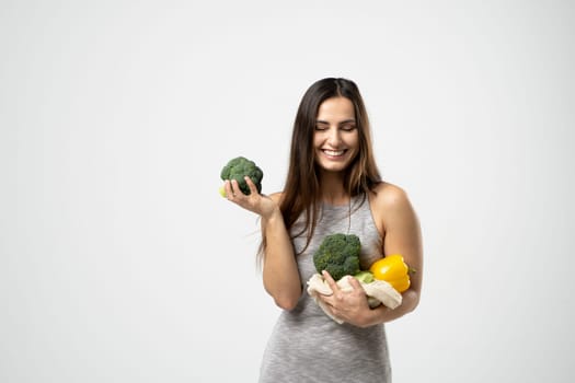 Smiling brunette girl is holding a broccoli and mesh shopping bag with vegetables, greens without plastic bags. Zero waste, plastic free Eco friendly concept. Sustainable lifestyle