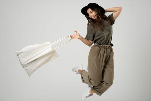 Zero waste concept. Happy young brunette woman in a green t-shirt and black hat jump with a cotton bag with groceries. Eco friendly lifestyle. Mockup