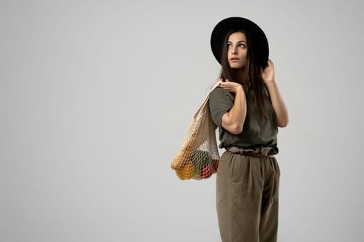 Zero waste concept. A young girl holds on her shoulder a textile mesh eco bag with a groceries. The girl smiles, wearing a beige t-shirt and hat. Refusal of plastic bags