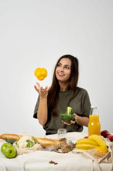 Happy woman in green t-shirt unpacking shopping mesh eco bag with healthy vegetables, fruits, bread, snacks on the kitchen at home. Healthy eating vegetarian concept