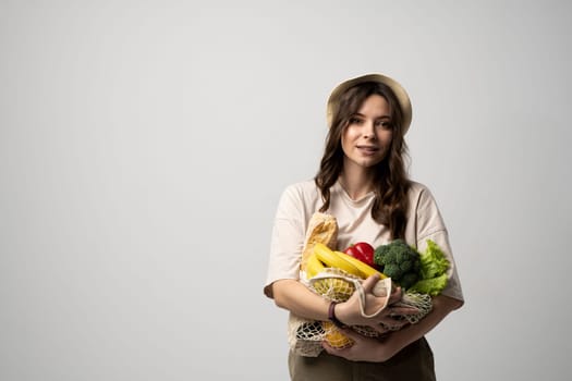 Zero waste concept. Young brunette woman holding reusable cotton shopping mesh bag with organic groceries from a market. Concept of no plastic. Zero waste, plastic free. Sustainable lifestyle