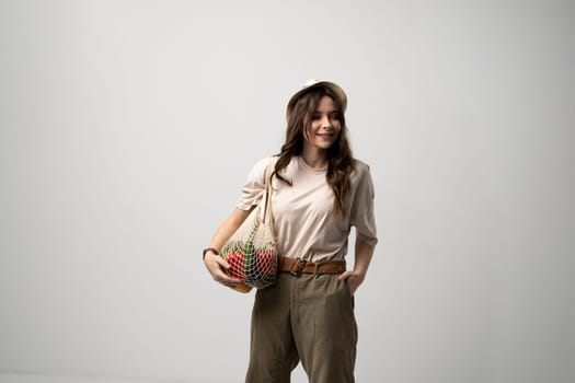 Zero waste concept. A young girl holds on her shoulder a textile mesh eco bag with a groceries. The girl smiles, wearing a beige t-shirt and hat. Refusal of plastic bags