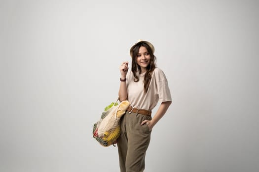 Concept of no plastic. Zero waste, plastic free. Sustainable lifestyle. Happy woman in a beige t-shirt and a hat holding reusable cotton shopping bag with organic groceries, bread and greens