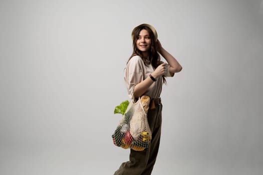 Concept of no plastic. Zero waste, plastic free. Sustainable lifestyle. Happy woman in a beige t-shirt and a hat holding reusable cotton shopping bag with organic groceries, bread and greens