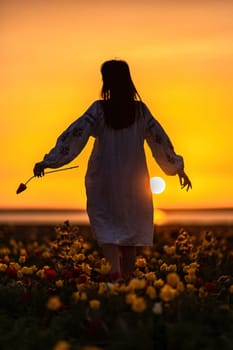 Woman back against sunset and wild tulip flowers, natural seasonal background. Multi-colored tulips Tulipa schrenkii in their natural habitat are listed in the Red Book