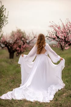 Woman peach blossom. Happy curly woman in white dress walking in the garden of blossoming peach trees in spring.