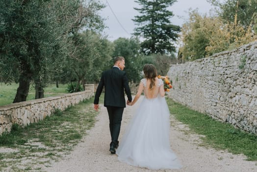 Happy stylish smiling couple walking in Tuscany, Italy on their wedding day. The bride and groom walk down the street by the hands. A stylish young couple walks. Husband and wife communicate nicely. Lovers run through the streets of the city.