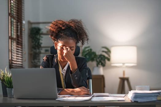 Young African American woman with afro hairstyle looks annoyed and stressed, sitting at the desk, using a laptop, thinking and looking at the camera, feeling tired and bored with depression problems..