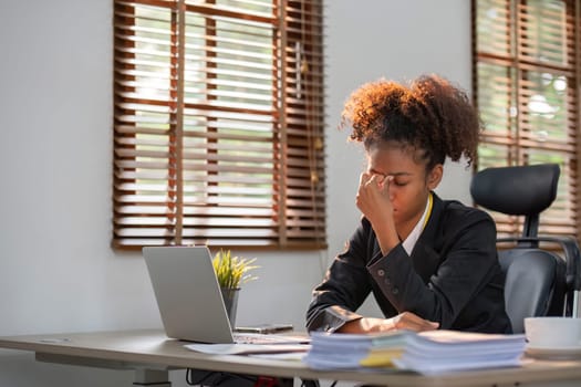 Young African American woman with afro hairstyle looks annoyed and stressed, sitting at the desk, using a laptop, thinking and looking at the camera, feeling tired and bored with depression problems..