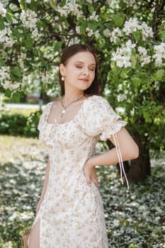 An attractive long-haired woman walks in the spring in the park of blooming apple trees. Spring portrait of a woman