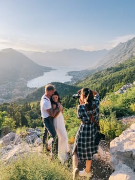 Girl-photographer photographs the bride and groom standing on a rock above the Kotor Bay. High quality photo
