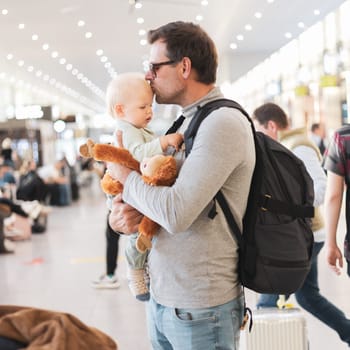 Father traveling with child, holding his infant baby boy at airport terminal waiting to board a plane. Travel with kids concept