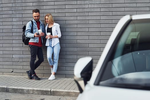 Young stylish man with woman in casual clothes outdoors near white car together. Conception of friendship or relationships.