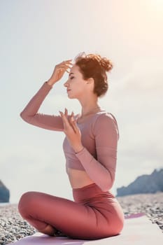 Young woman with long hair in white swimsuit and boho style braclets practicing outdoors on yoga mat by the sea on a sunset. Women's yoga fitness routine. Healthy lifestyle, harmony and meditation