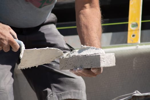 close up of the hands of a bricklayer applying cement mortar to a brick to stick it into the masonry for building a house, High quality photo