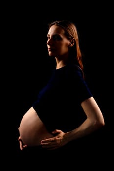 Beautiful pregnant woman over black background. Artistic low key light in studio. High quality photo