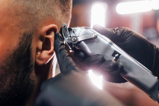 Close up view of young bearded man that sitting and getting haircut in barber shop.