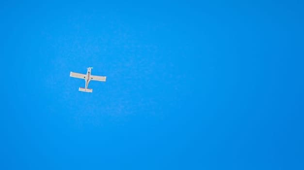 A small light plane flies in the clear sky. View from below. Horizontal orientation