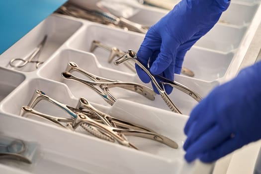 Doctor's hand wearing a disposable medical gloves holding a stainless steel nasal speculum for ENT examination over other surgery instruments