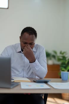 Burnout American African business man in stress works with many paperwork document, migraine attack, Freelance, work from home.