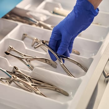 Doctor's hand wearing a disposable medical gloves holding a stainless steel nasal speculum for ENT examination over other surgery instruments