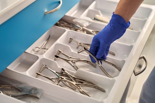 Doctor's hand wearing a disposable medical gloves holding a stainless steel nasal speculum for ENT examination over other surgery instruments