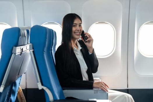 Successful young business woman working speaking on mobile phone while while sitting on aircraft cabinin.