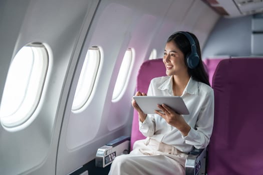 Young Asian business woman or female passenger wearing wireless headphone and working with tablet during the flight.