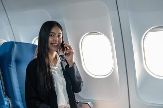 Successful young business woman working speaking on mobile phone while while sitting on aircraft cabinin.