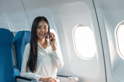 Successful young business woman working speaking on mobile phone while while sitting on aircraft cabinin.