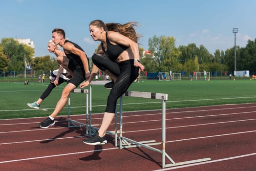 Two athlete woman and man runnner running hurdles at the stadium outdoors