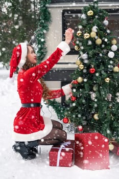 Young woman in santa costume decorates the Christmas tree at winter campsite getting ready for the new year. New year celebration concept